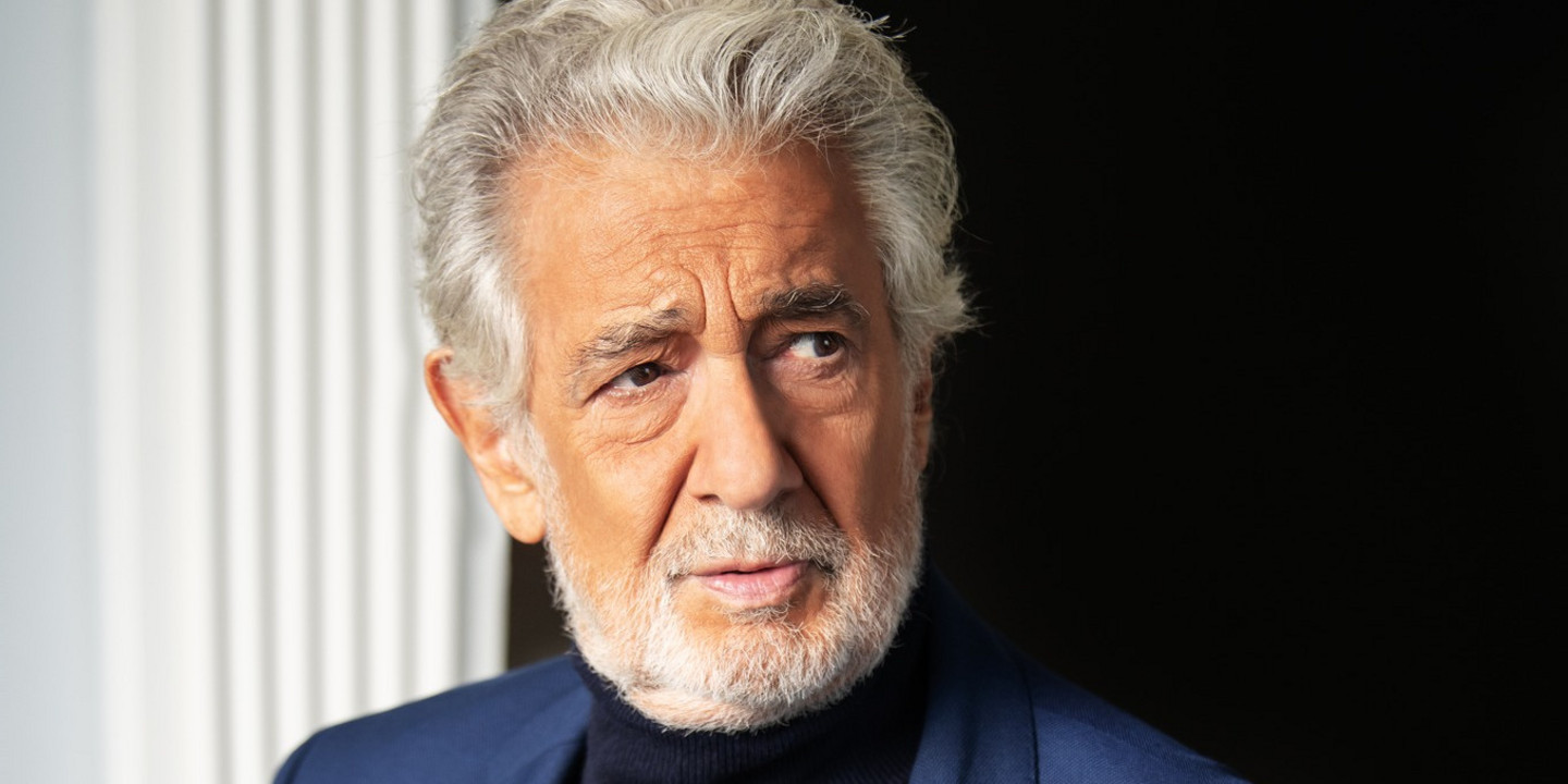 Porträt eines älteren Mannes mit grauem Haar und Bart, in blauem Sakko und dunklem Rollkragenpullover, seitlich blickend vor hellem Fenster und dunklem Hintergrund.