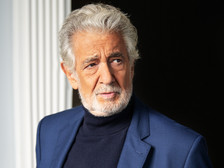 Porträt eines älteren Mannes mit grauem Haar und Bart, in blauem Sakko und dunklem Rollkragenpullover, seitlich blickend vor hellem Fenster und dunklem Hintergrund.