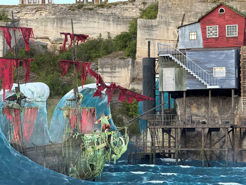 © Adam Kürth, klassikticket.at Nahaufnahme des Bühnenbilds mit einem verfallenen Geisterschiff, roten zerfetzten Segeln und Darstellern in aufwändiger Kostümierung.