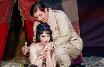 © Christian Husar Sängerin sitzt emotional bewegt am Boden, während ein Mann in beiger Uniform sie tröstend umarmt – Szene aus einer Opern- oder Operettenaufführung mit orientalisch inspiriertem Bühnenbild.