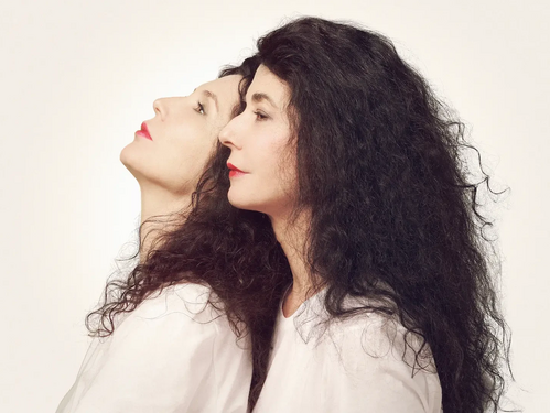 © Umberto Nicoletti Künstlerporträt der Pianistinnen Katia und Marielle Labèque, im Profil Rücken an Rücken, mit weißen Oberteilen vor hellem Hintergrund.