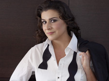 Cecilia Bartoli im weißen Hemd mit offenem Smokinghemd und schwarzer Fliege, die Jacke lässig über die Schulter gelegt, vor dunklem Hintergrund.