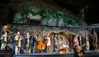 © Franz Neumayr Junge Musiker:innen in traditionellen Gewändern musizieren mit Geigen, Kontrabass, Zither, Akkordeon und Gitarre vor einer Bühnenkulisse mit Weinreben und Bergen beim Salzburger Adventsingen.