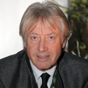 © www.salzburgeradvent.at Porträt von E. W. Holzmann im Anzug und schwarzer Krawatte, der direkt in die Kamera schaut; im Hintergrund unscharfes Grün.