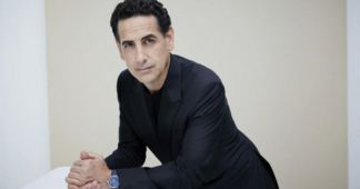 © Gregor Hohenberg Ein Mann in dunklem Anzug lehnt sich leicht nach vorne und blickt direkt in die Kamera. Der Hintergrund ist hell und schlicht gehalten.