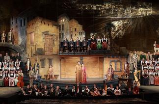 Große Bühnenaufnahme des Salzburger Adventsingens mit Chor, Orchester und Solisten in historischen Kostümen, vor einer detailreichen Kulissenlandschaft, die ein Dorf mit Häusern und Bögen darstellt.