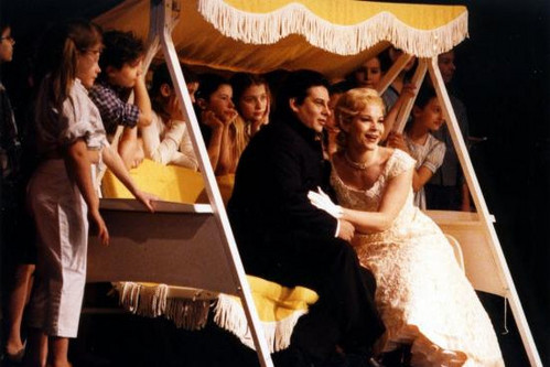 © ZDF und ORF Opernszene mit Sängerin im hellen Kleid und Sänger auf einer Bühne mit Kindern und Bühnenrequisite.