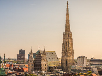 Panoramablick über Wien mit dem Stephansdom als markanter Turm in der Mitte, umgeben von historischen Dächern und modernen Gebäuden im warmen Abendlicht.