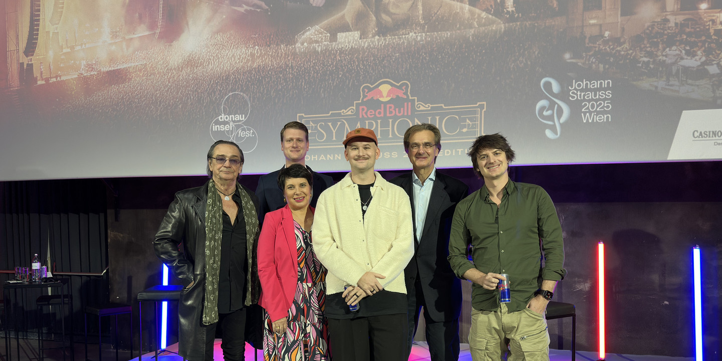 Sechs Menschen posieren lächelnd vor Red Bull Symphonic Plakat.