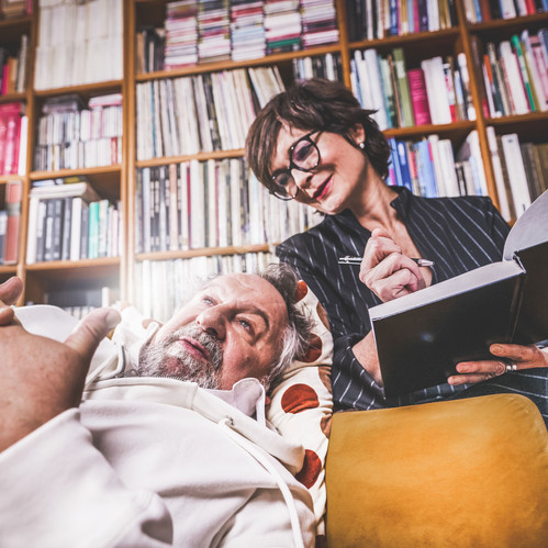 © Daniela Matejschek Ein älterer Mann liegt nachdenklich auf einer Couch, während eine Frau mit Notizbuch und Stift neben ihm sitzt und aufmerksam lächelt – Szene wirkt wie eine Therapiesitzung.