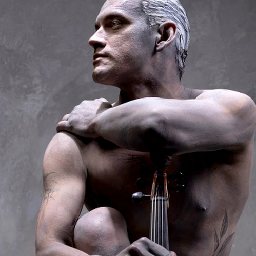 Ein nackter Mann sitzt skulptural mit einer Viola da gamba vor dem Körper und blickt seitlich nach oben.