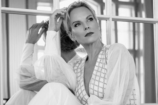 © Sarah Katharina Photography Schwarzweiß-Porträt einer elegant gekleideten Frau im hellen Kleid, sitzend vor einem Spiegel und nachdenklich zur Seite blickend.